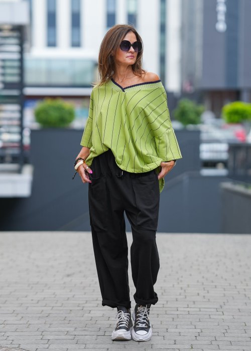 Czarne spodnie damskie o luźnym kroju z elastycznym pasem i dużymi naszywanymi kieszeniami z przodu. Model zestawiony ze sneakersami i zieloną bluzą w paski w miejskiej stylizacji