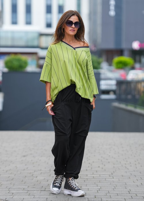 Czarne spodnie damskie o luźnym kroju z elastycznym pasem i dużymi naszywanymi kieszeniami z przodu. Model zestawiony ze sneakersami i zieloną bluzą w paski w miejskiej stylizacji