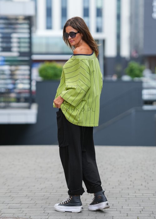 Czarne spodnie damskie o luźnym kroju z elastycznym pasem i dużymi naszywanymi kieszeniami z przodu. Model zestawiony ze sneakersami i zieloną bluzą w paski w miejskiej stylizacji