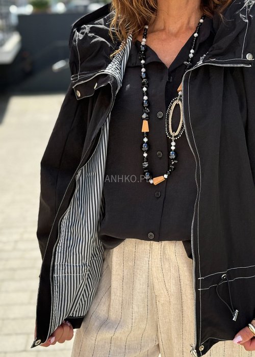 Czarna kurtka damska oversize z kapturem i kontrastowymi przeszyciami, pokazana w miejskiej stylizacji. Model zapinany na suwak, o luźnym kroju, zestawiony z jasnymi spodniami.