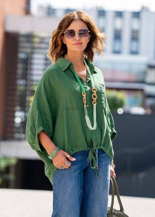 Zielona koszula lniana damska o luźnym kroju z kołnierzykiem i kieszonką, zestawiona z jeansami i biżuterią w naturalnym stylu, prezentująca swobodny look.