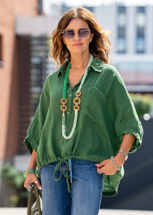 Zielona koszula lniana damska o luźnym kroju z kołnierzykiem i kieszonką, zestawiona z jeansami i biżuterią w naturalnym stylu, prezentująca swobodny look.