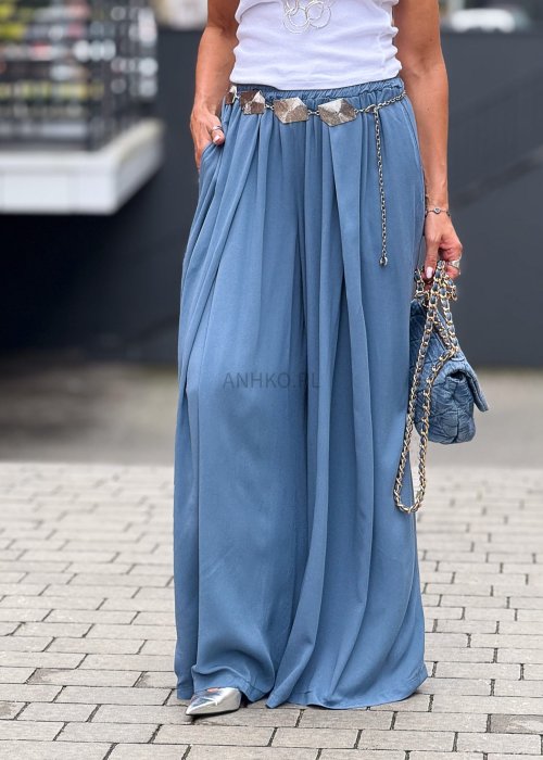 Niebieskie spodnie damskie z szeroką, lejącą nogawką i elastycznym pasem, stylizowane z białą bluzką i dodatkami w eleganckim, miejskim stylu.
