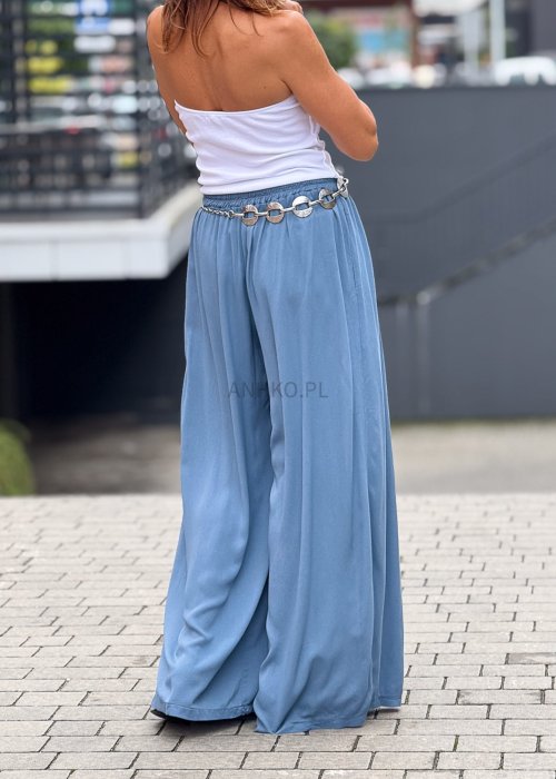 Niebieskie spodnie damskie z szeroką, lejącą nogawką i elastycznym pasem, stylizowane z białą bluzką i dodatkami w eleganckim, miejskim stylu.