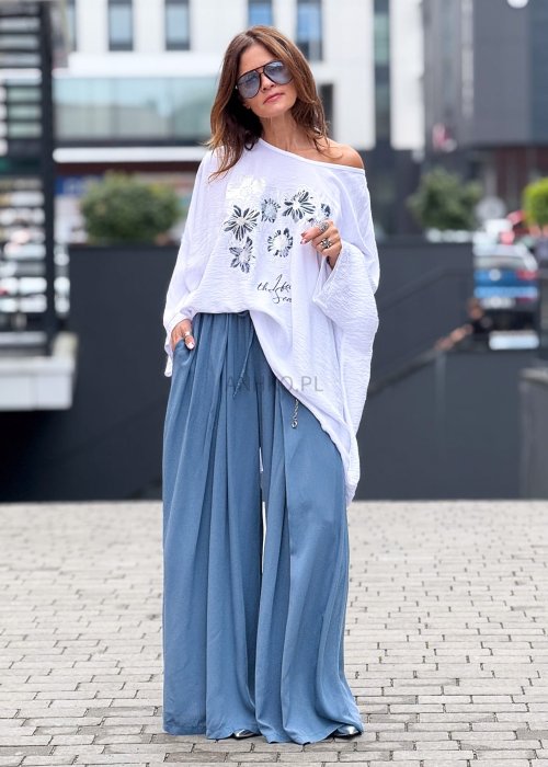 Niebieskie spodnie damskie z szeroką, lejącą nogawką i elastycznym pasem, stylizowane z białą bluzką i dodatkami w eleganckim, miejskim stylu.