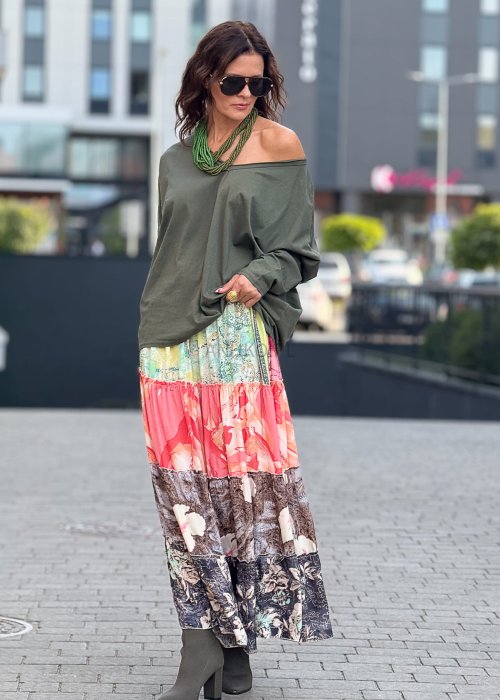 Khaki bluzka damska oversize z długim rękawem i dekoltem V, stylizowana lekko opuszczona na ramię. Model prezentowany ze wzorzystą spódnicą midi i naszyjnikiem w zielonym kolorze.