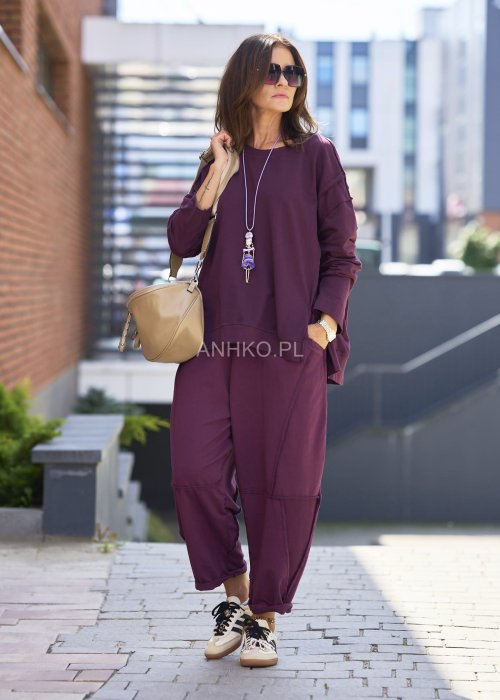 Śliwkowa bluza damska oversize z długim rękawem i okrągłym dekoltem, zestawiona z zieloną spódnicą i biżuterią w stylu miejskim.