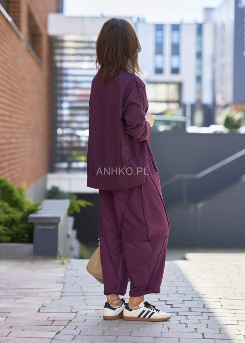 Śliwkowa bluza damska oversize z długim rękawem i okrągłym dekoltem, zestawiona z zieloną spódnicą i biżuterią w stylu miejskim.