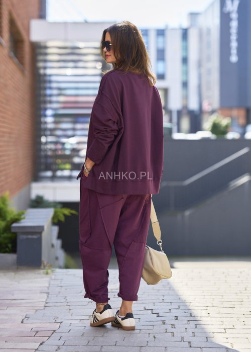 Śliwkowa bluza damska oversize z długim rękawem i okrągłym dekoltem, zestawiona z zieloną spódnicą i biżuterią w stylu miejskim.