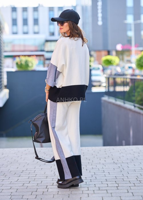 Damski komplet w stylu casual – oversizowa bluzka z szerokimi rękawami w kolorze biało–szaro–czarnym, ozdobiona broszkami przy mankietach, zestawiona z dopasowanymi spodniami w tej samej kolorystyce
