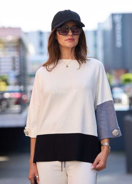 Damski komplet w stylu casual – oversizowa bluzka z szerokimi rękawami w kolorze biało–szaro–czarnym, ozdobiona broszkami przy mankietach, zestawiona z dopasowanymi spodniami w tej samej kolorystyce