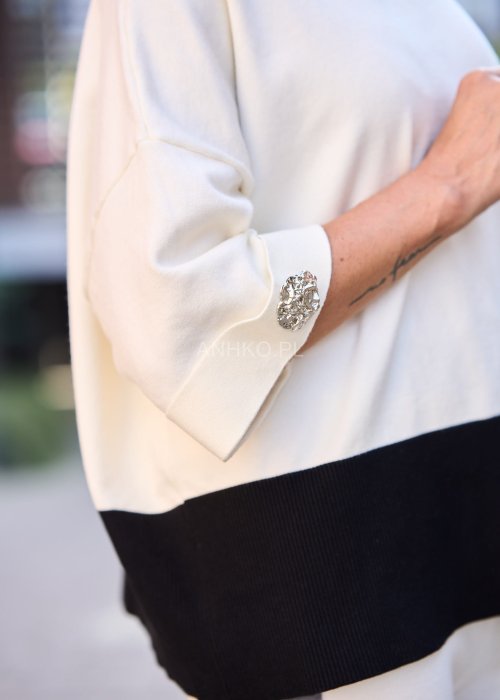 Damski komplet w stylu casual – oversizowa bluzka z szerokimi rękawami w kolorze biało–szaro–czarnym, ozdobiona broszkami przy mankietach, zestawiona z dopasowanymi spodniami w tej samej kolorystyce