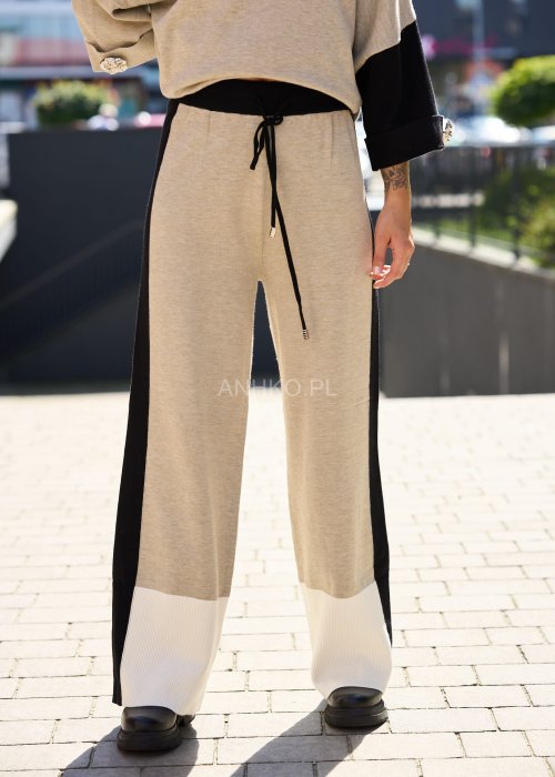 Damski beżowy komplet dresowy – luźna bluza z szerokimi rękawami i kontrastowymi czarnymi wstawkami, zestawiona ze spodniami z szerokimi nogawkami, wykończonymi białymi panelami
