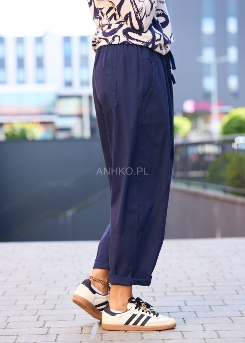 Granatowe spodnie damskie o luźnym kroju boyfriend z elastycznym pasem i troczkiem, pokazane w codziennej stylizacji ze sneakersami. Model ma zwężaną nogawkę, boczne kieszenie i swobodnie układa się na sylwetce.