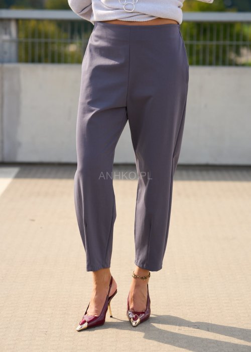 Ciemnoszare spodnie damskie typu cygaretki z elastycznym pasem i zwężaną nogawką, zestawione ze szpilkami w eleganckiej stylizacji miejskiej.