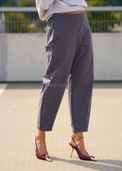 Ciemnoszare spodnie damskie typu cygaretki z elastycznym pasem i zwężaną nogawką, zestawione ze szpilkami w eleganckiej stylizacji miejskiej.