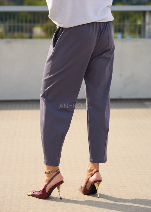 Ciemnoszare spodnie damskie typu cygaretki z elastycznym pasem i zwężaną nogawką, zestawione ze szpilkami w eleganckiej stylizacji miejskiej.