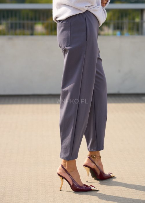 Ciemnoszare spodnie damskie typu cygaretki z elastycznym pasem i zwężaną nogawką, zestawione ze szpilkami w eleganckiej stylizacji miejskiej.