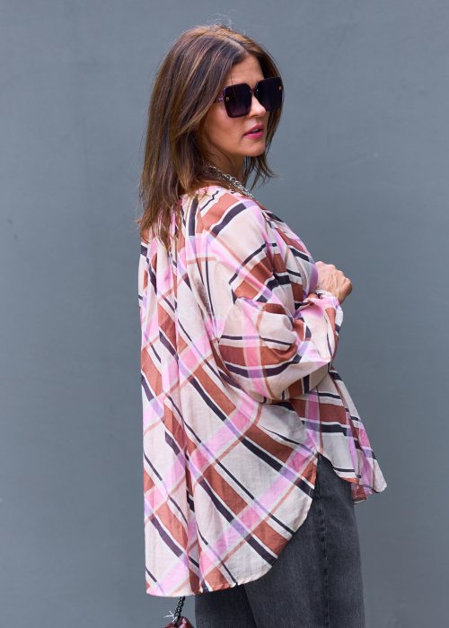 Wzorzysta bluzka w różowo-brązową kratę, kremowe spodnie i brązowy pasek, do tego duże okulary i delikatny naszyjnik.