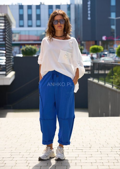 Niebieskie damskie spodnie dresowe o luźnym kroju z ozdobnymi przeszyciami i wiązaniem w pasie. Model z kieszeniami, pokazany w codziennej stylizacji ze sneakersami.