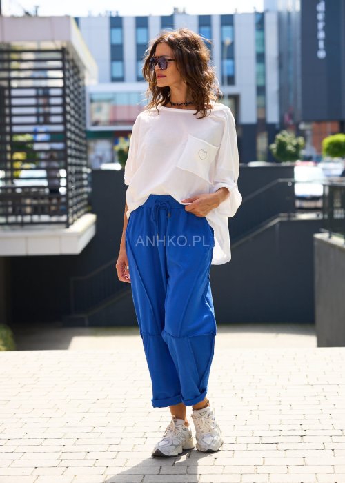 Niebieskie damskie spodnie dresowe o luźnym kroju z ozdobnymi przeszyciami i wiązaniem w pasie. Model z kieszeniami, pokazany w codziennej stylizacji ze sneakersami.