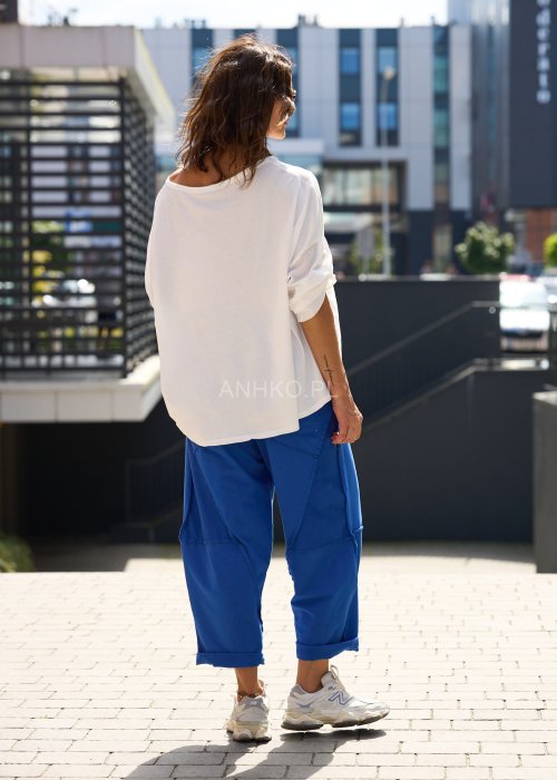 Niebieskie damskie spodnie dresowe o luźnym kroju z ozdobnymi przeszyciami i wiązaniem w pasie. Model z kieszeniami, pokazany w codziennej stylizacji ze sneakersami.