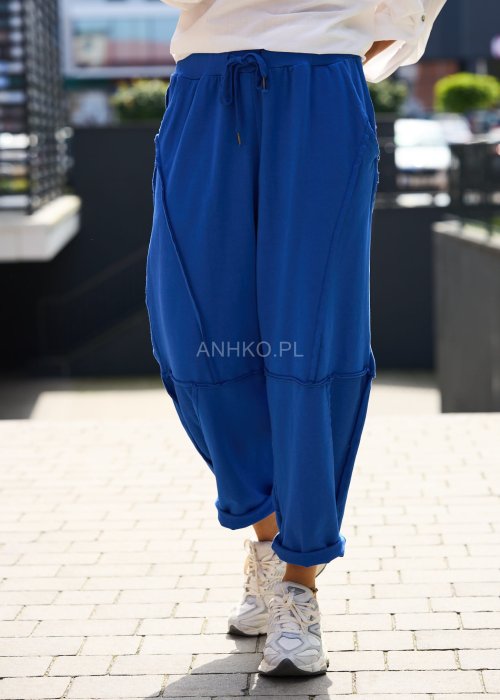 Niebieskie damskie spodnie dresowe o luźnym kroju z ozdobnymi przeszyciami i wiązaniem w pasie. Model z kieszeniami, pokazany w codziennej stylizacji ze sneakersami.