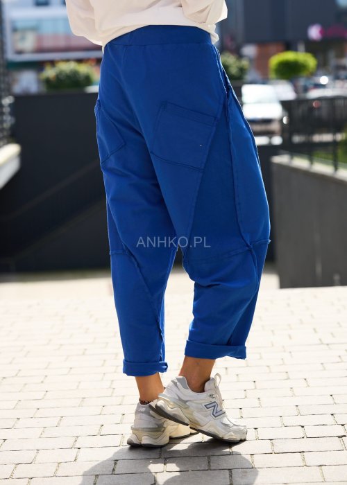 Niebieskie damskie spodnie dresowe o luźnym kroju z ozdobnymi przeszyciami i wiązaniem w pasie. Model z kieszeniami, pokazany w codziennej stylizacji ze sneakersami.