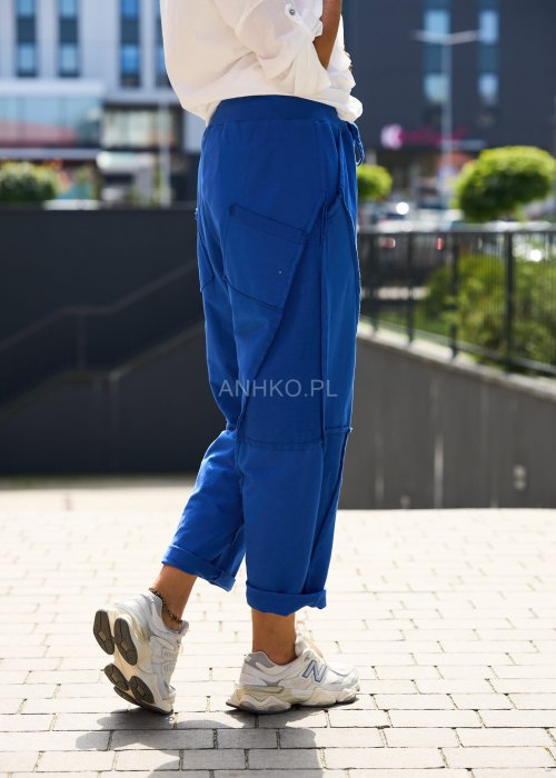 Niebieskie damskie spodnie dresowe o luźnym kroju z ozdobnymi przeszyciami i wiązaniem w pasie. Model z kieszeniami, pokazany w codziennej stylizacji ze sneakersami.