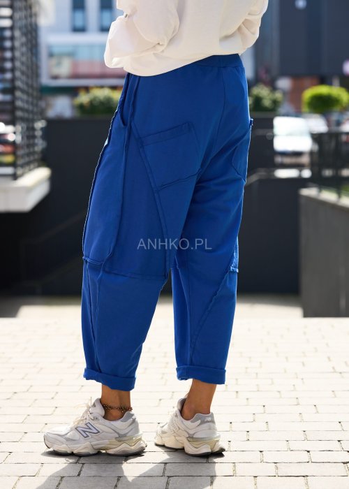 Niebieskie damskie spodnie dresowe o luźnym kroju z ozdobnymi przeszyciami i wiązaniem w pasie. Model z kieszeniami, pokazany w codziennej stylizacji ze sneakersami.