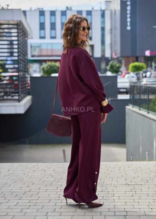 Śliwkowe spodnie damskie z szeroką nogawką i ozdobnymi złotymi guzikami przy dole nogawek