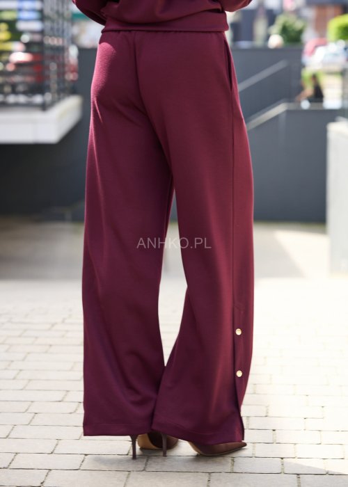 Śliwkowe spodnie damskie z szeroką nogawką i ozdobnymi złotymi guzikami przy dole nogawek