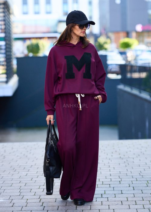 Burgundowy komplet dresowy damski z oversize’ową bluzą z literą M i szerokimi spodniami z elastycznym pasem, stylizacja w miejskim klimacie z czapką z daszkiem.