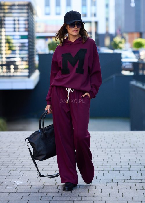 Burgundowy komplet dresowy damski z oversize’ową bluzą z literą M i szerokimi spodniami z elastycznym pasem, stylizacja w miejskim klimacie z czapką z daszkiem.