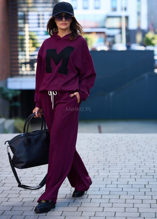 Burgundowy komplet dresowy damski z oversize’ową bluzą z literą M i szerokimi spodniami z elastycznym pasem, stylizacja w miejskim klimacie z czapką z daszkiem.