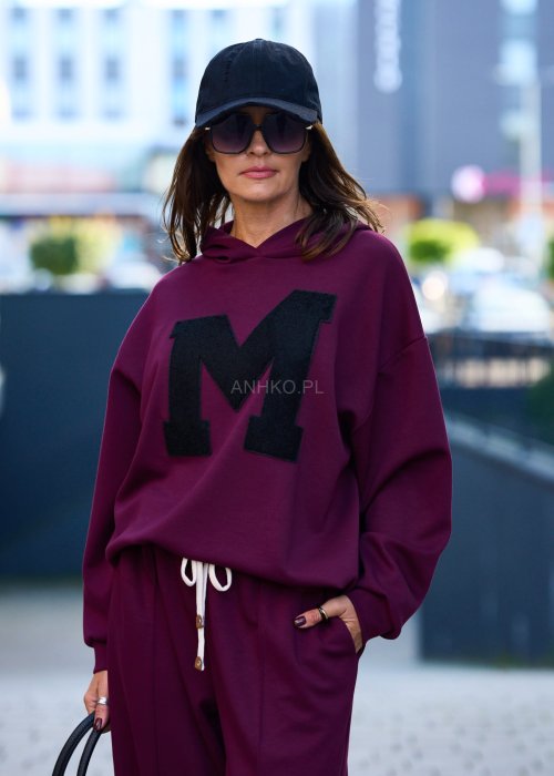 Burgundowy komplet dresowy damski z oversize’ową bluzą z literą M i szerokimi spodniami z elastycznym pasem, stylizacja w miejskim klimacie z czapką z daszkiem.