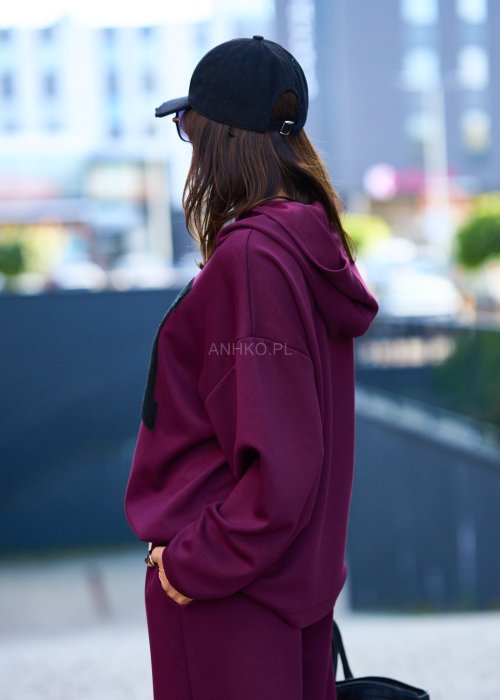 Burgundowy komplet dresowy damski z oversize’ową bluzą z literą M i szerokimi spodniami z elastycznym pasem, stylizacja w miejskim klimacie z czapką z daszkiem.