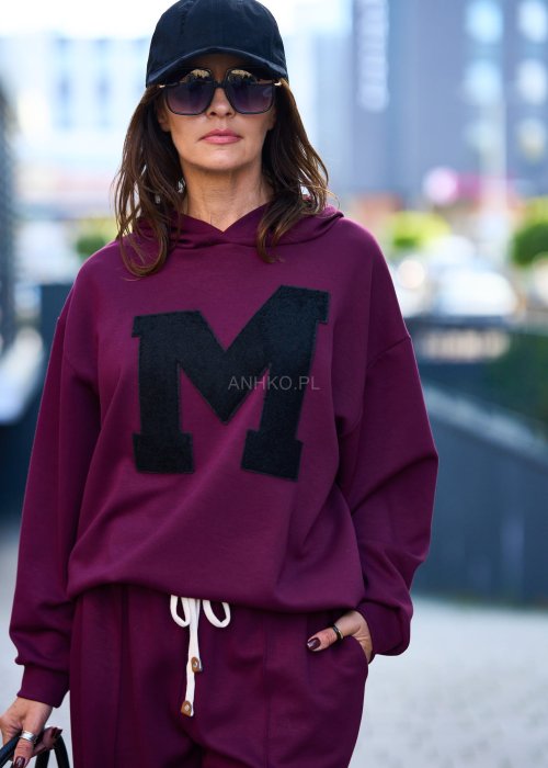 Burgundowy komplet dresowy damski z oversize’ową bluzą z literą M i szerokimi spodniami z elastycznym pasem, stylizacja w miejskim klimacie z czapką z daszkiem.