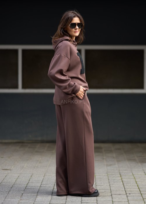 Brązowy komplet dresowy damski z oversize’ową bluzą z literą M i szerokimi spodniami z elastycznym pasem, stylizacja w nowoczesnym miejskim klimacie