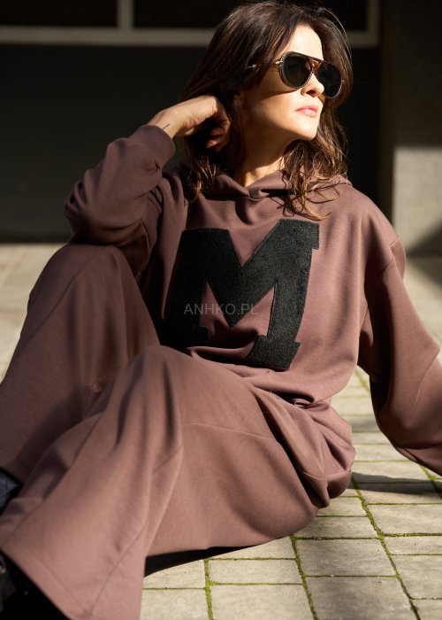 Brązowy komplet dresowy damski z oversize’ową bluzą z literą M i szerokimi spodniami z elastycznym pasem, stylizacja w nowoczesnym miejskim klimacie