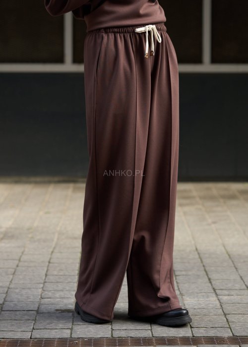 Brązowy komplet dresowy damski z oversize’ową bluzą z literą M i szerokimi spodniami z elastycznym pasem, stylizacja w nowoczesnym miejskim klimacie