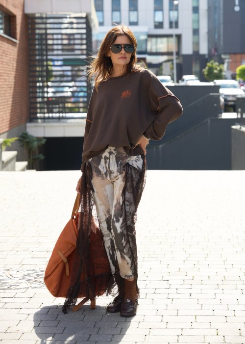 Damskie spodnie w odcieniach brązu i beżu, z nałożoną koronkową warstwą z ciemnobrązowej siateczki, stylizowane z brązowymi mokasynami i skarpetkami.