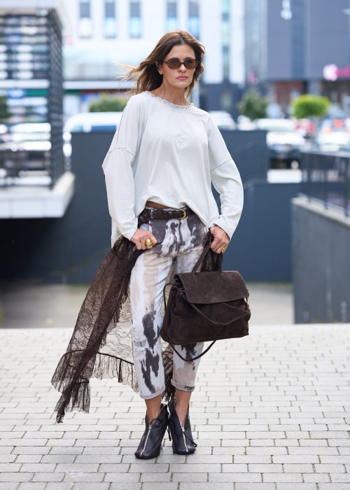 Damskie spodnie w odcieniach brązu i beżu, z nałożoną koronkową warstwą z ciemnobrązowej siateczki, stylizowane z brązowymi mokasynami i skarpetkami.