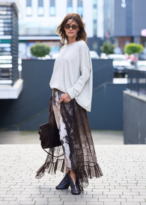 Damskie spodnie w odcieniach brązu i beżu, z nałożoną koronkową warstwą z ciemnobrązowej siateczki, stylizowane z brązowymi mokasynami i skarpetkami.