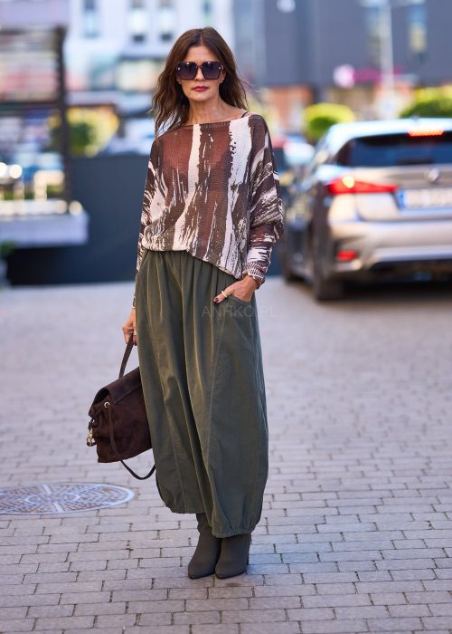 Spódnica maxi w kolorze khaki z elastyczną talią i kieszeniami, o luźnym kroju, zestawiona z wzorzystą bluzką i botkami na słupku w miejskiej stylizacji.