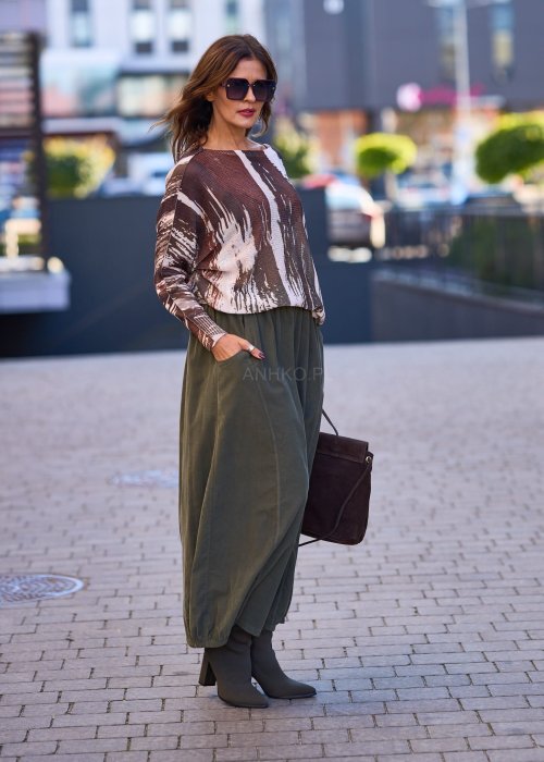 Spódnica maxi w kolorze khaki z elastyczną talią i kieszeniami, o luźnym kroju, zestawiona z wzorzystą bluzką i botkami na słupku w miejskiej stylizacji.