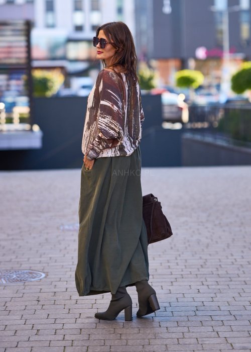 Spódnica maxi w kolorze khaki z elastyczną talią i kieszeniami, o luźnym kroju, zestawiona z wzorzystą bluzką i botkami na słupku w miejskiej stylizacji.