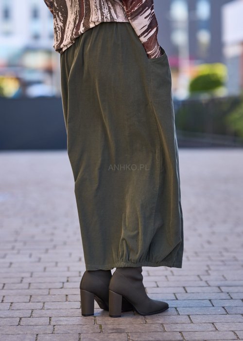 Spódnica maxi w kolorze khaki z elastyczną talią i kieszeniami, o luźnym kroju, zestawiona z wzorzystą bluzką i botkami na słupku w miejskiej stylizacji.