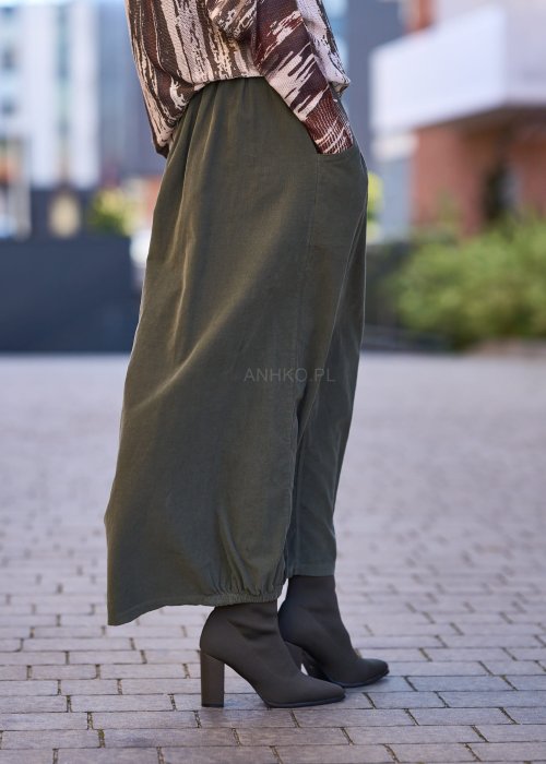 Spódnica maxi w kolorze khaki z elastyczną talią i kieszeniami, o luźnym kroju, zestawiona z wzorzystą bluzką i botkami na słupku w miejskiej stylizacji.