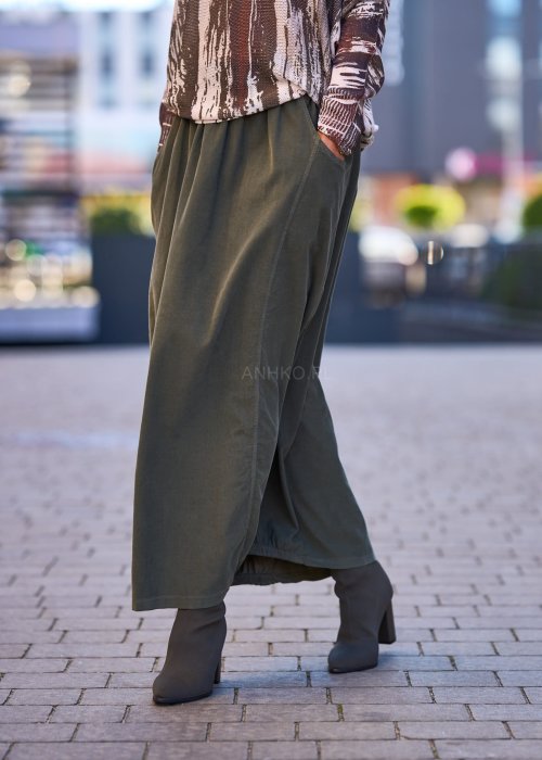 Spódnica maxi w kolorze khaki z elastyczną talią i kieszeniami, o luźnym kroju, zestawiona z wzorzystą bluzką i botkami na słupku w miejskiej stylizacji.